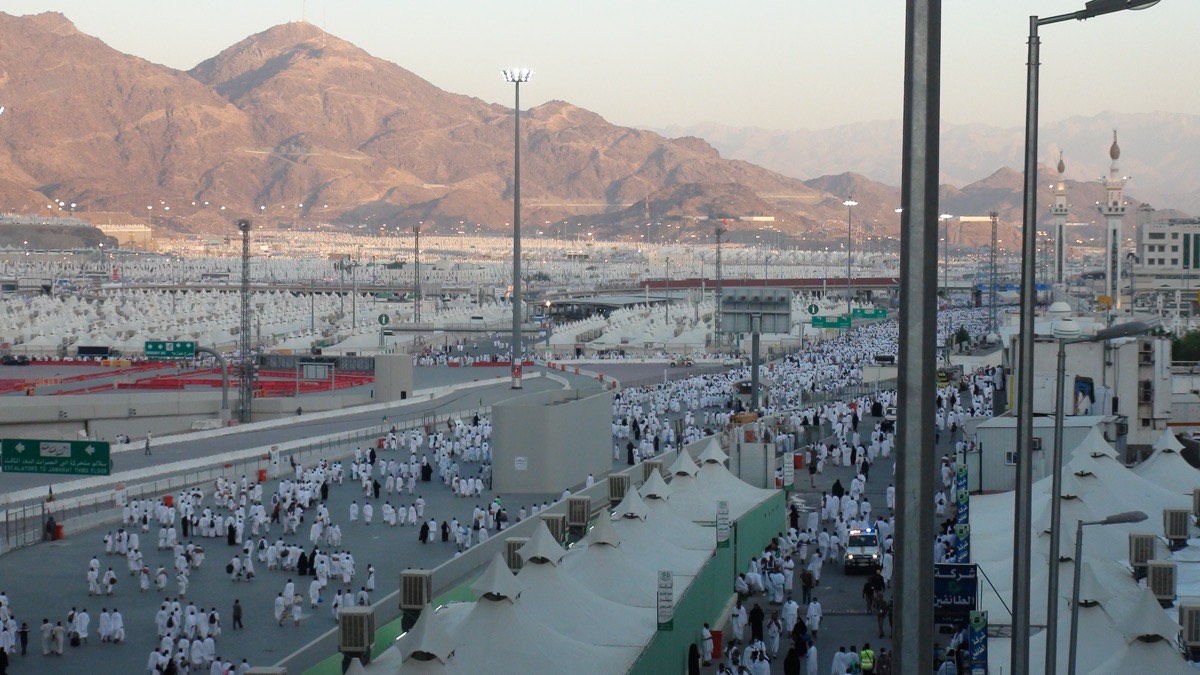Mina at first light: white tents filling the valley to the bare hills, with pilgrims in ihram walking the road towards the Jamarat.
